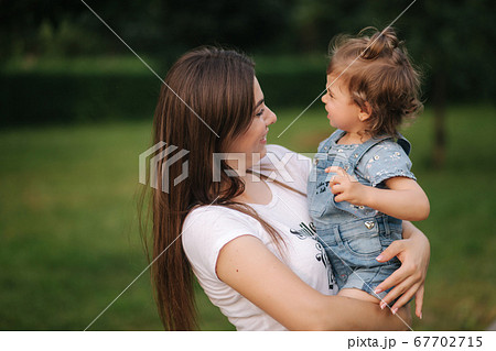 Portrait of beautiful mom with adorable little girl. Happy family outdoors. Daughter look at mom 67702715