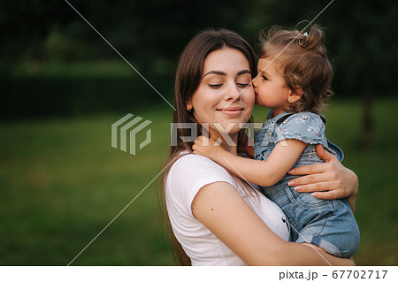 Portrait of beautiful mom with adorable little girl. Happy family outdoors. Daughter give kiss to mom 67702717