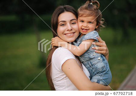Portrait of beautiful mom with adorable little girl. Happy family outdoors. Daughter hug mum 67702718