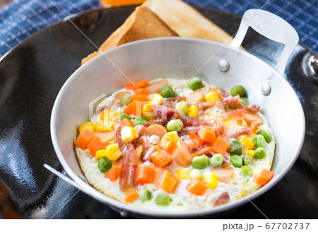 breakfast with fried eggs in a pan with bacon and vegetables on dark plate. 67702737