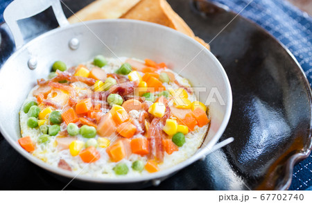 breakfast with fried eggs in a pan with bacon and vegetables on dark plate. 67702740