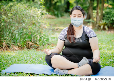 Asian fat girl doing yoga meditation at outdoor public green park and wear face mask  67705916