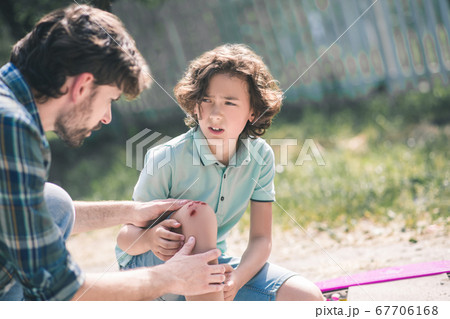 Man in a checkered shirt examining his sons injured knee 67706168