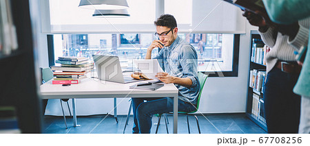 Handsome young male freelancer in spectacles reading information Handsome young male freelancer in spectacles reading information 67708256