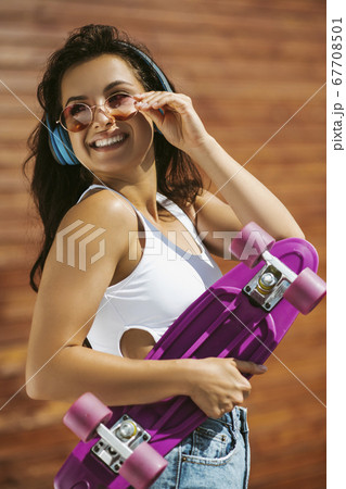 Beautiful brunette girl holding a skateboard and smiling Beautiful brunette girl holding a skateboard and smiling 67708501