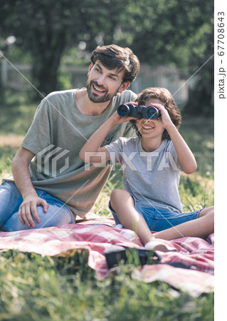 Dark-haired boy sitting next to his dad watching binoculars, looking interested Dark-haired boy sitting next to his dad watching binoculars, looking interested 67708643
