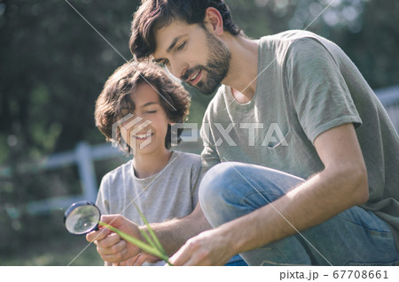 Dark-haired boy and his dad looking at the plant through magnifying glass 67708661
