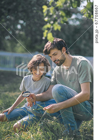 Dark-haired boy and his father looking at the plant through magnifying glass and looking interested Dark-haired boy and his father looking at the plant through magnifying glass and looking interested 67708667