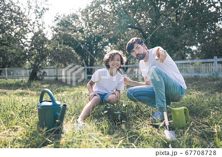 Dark-haired man and his son sitting on the grass, father showing something 67708728