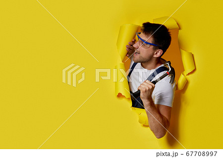 worker holding hammer through hole in yellow paper. worker holding hammer through hole in yellow paper. 67708997