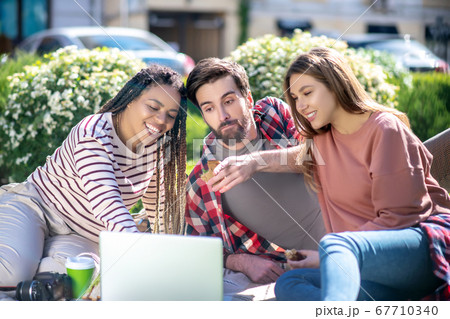 Interested guy and smiling girls on picnic in front of laptop 67710340