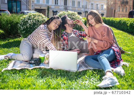 Three friends on a picnic with a laptop Three friends on a picnic with a laptop 67710342