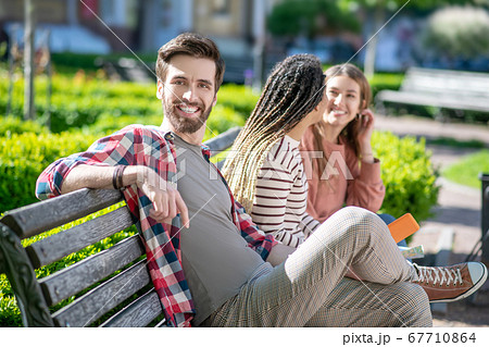 Young attractive guy posing and two girls on bench. 67710864