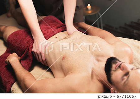 Male masseur massages the thoracic diaphragm of a muscular male athlete in a massage room with dark lighting 67711067