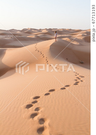 Blonde female Caucasian traveler leaving footprints in sand dunes when walking in dessert in Oman Blonde female Caucasian traveler leaving footprints in sand dunes when walking in dessert in Oman 67713193