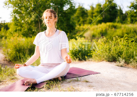 Young woman meditating sitting in lotus pose with closed eyes, holding hand in Om position on knee. 67714256