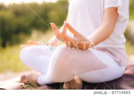 Close-up of unrecognizable woman sitting in lotus position and holding finger hand in Om position. Close-up of unrecognizable woman sitting in lotus position and holding finger hand in Om position. 67714605