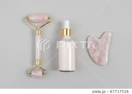 Crystal rose quartz facial roller, massage tool Gua sha and anti-aging collagen, serum in glass bottle on grey background. Facial massage for natural lifting, Beauty concept Top view Crystal rose quartz facial roller, massage tool Gua sha and anti-aging collagen, serum in glass bottle on grey background. Facial massage for natural lifting, Beauty concept Top view 67717526