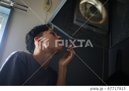 換気扇の下でタバコを吸う男性 67717915