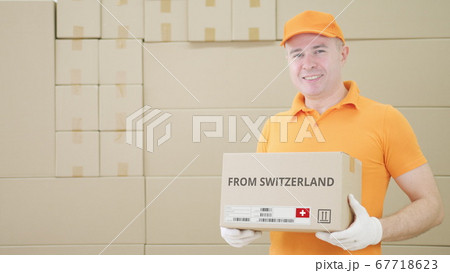 Man holding cardboard parcel with printed FROM SWITZERLAND text on it 67718623