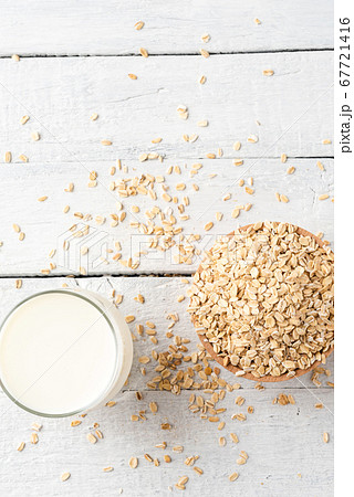 Overhead shot of glass of oat milk on white wooden background with oatmeals in bowl 67721416
