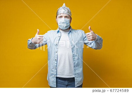 Man protected himself from the virus, put on a medical mask and a tin foil hat, he makes a thumbs up 67724589