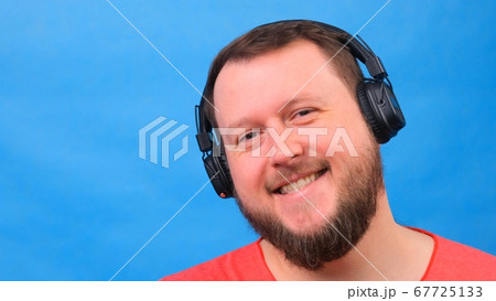 Bearded funny smiling cute fat man in a pink T-shirt listens to music and dances on a blue Bearded funny smiling cute fat man in a pink T-shirt listens to music and dances on a blue 67725133