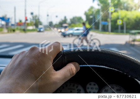 a man hand on the steering wheel of a car in front of a pedestrian crossing a man hand on the steering wheel of a car in front of a pedestrian crossing 67730621