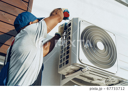 Repairman in uniform installing the outside unit of air conditioner 67733712