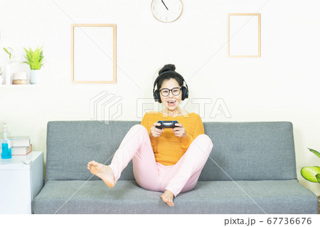 people and leisure concept - happy smiling asian young woman with gamepad playing video games on console having fun, resting on weekends at home under quarantine people and leisure concept - happy smiling asian young woman with gamepad playing video games on console having fun, resting on weekends at home under quarantine 67736676