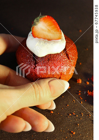The girl's hand holds a chocolate cupcake decorated with a strawberry slice The girl's hand holds a chocolate cupcake decorated with a strawberry slice 67745938
