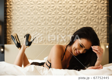 Foto de Beauty of woman body and lingerie concept. Beautiful brunette female  fashion model in sexy black underwear poses in luxury hotel room. Young  girl lies on a bed in bedroom wearing
