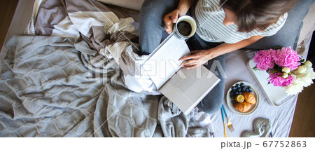 Woman sitting in bed reading a book and having breakfast. Top view 67752863