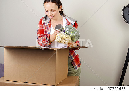 Unpacking the parcel. The woman opens the box and happily takes out the purchases from the online Unpacking the parcel. The woman opens the box and happily takes out the purchases from the online 67755683