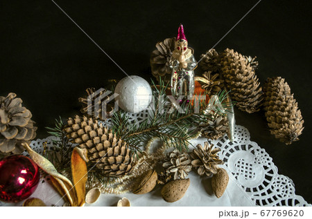 Corner openwork paper napkin with various coniferous cones, coniferous twig, Christmas toys, almonds and orange peels on  black background 67769620