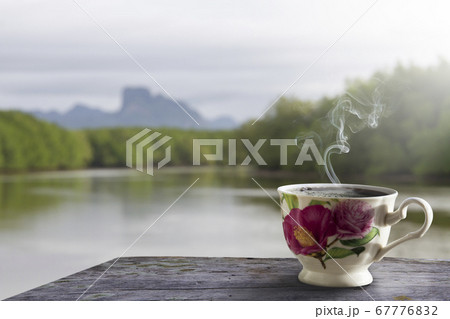 White floral hot coffee cups on a wooden table and a shining river view background 67776832