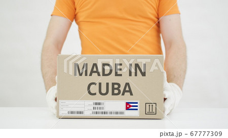 Man puts cardboard box with MADE IN CUBA text on the table Man puts cardboard box with MADE IN CUBA text on the table 67777309