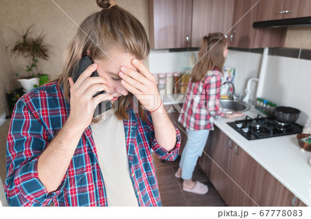 Serious disturbance long-haired young man standing in the kitchen uses his mobile phone or order a service from the Internet talking on the phone 67778083