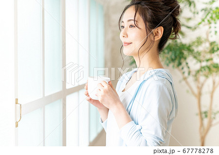 カップを持って窓辺に立つ若い女性 67778278