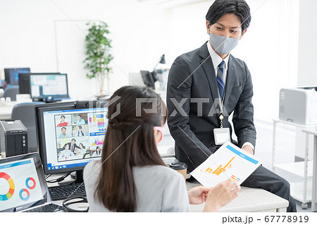 zoomで話をしながら社内で話をするマスクをつけた会社員2人 67778919
