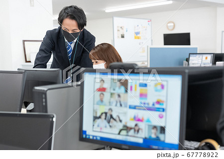 web会議 画面越しの会社にいるマスクをつけた会社員2人 67778922
