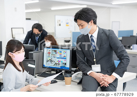 zoomで話をしながら社内で話をするマスクをつけた会社員 67778929