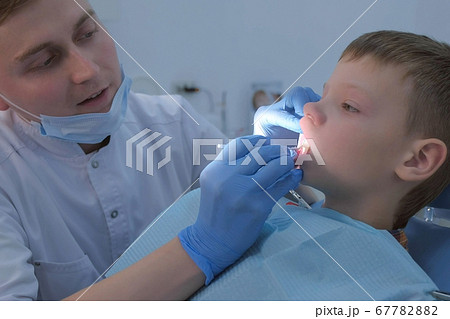 Dentist making fluoridation of boy's teeth after cleaning for protection. 67782882