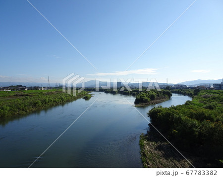 青空の日の川の合流地点と遠くに見える街と山のある景色 青空の日の川の合流地点と遠くに見える街と山のある景色 67783382