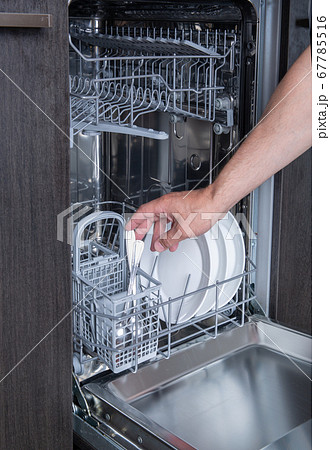 Housework open the dishwasher and the person puts the plate in the machine 67785516