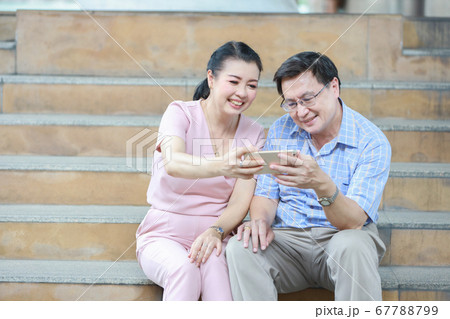 asian traveler couple in pink and blue shirt sitting on the stairs in downtown and using cell phone asian traveler couple in pink and blue shirt sitting on the stairs in downtown and using cell phone 67788799