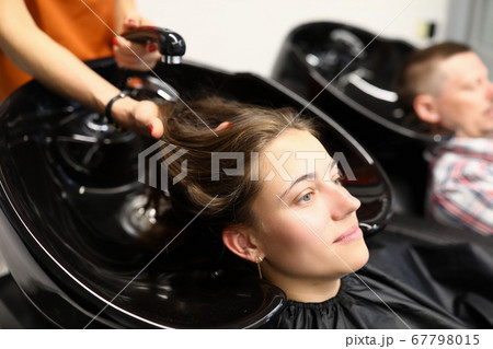 Client sit with head thrown back and hairdresser wash her hair in barber shop 67798015