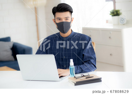 Young business man in face mask working from home with laptop computer. 67808629