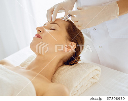 Beautiful woman receiving beauty injections with closed eyes. Beautician doctor hands doing beauty procedure to female face with syringe. Cosmetic medicine and surgery concept 67808930