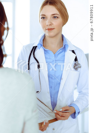 Young woman doctor and patient at medical examination at hospital office. Blue color blouse of therapist looks good. Medicine and healthcare concept Young woman doctor and patient at medical examination at hospital office. Blue color blouse of therapist looks good. Medicine and healthcare concept 67809911